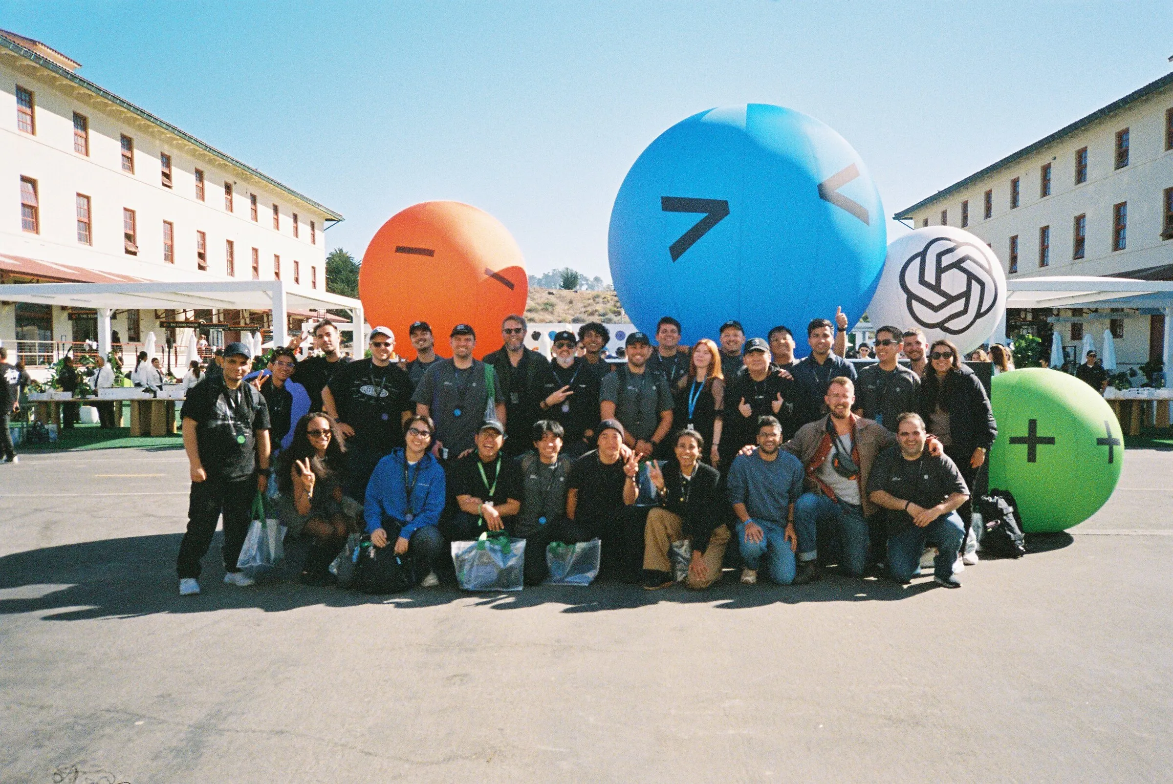 A large group posing outside a pavilion beside giant inflatable emoji balloons