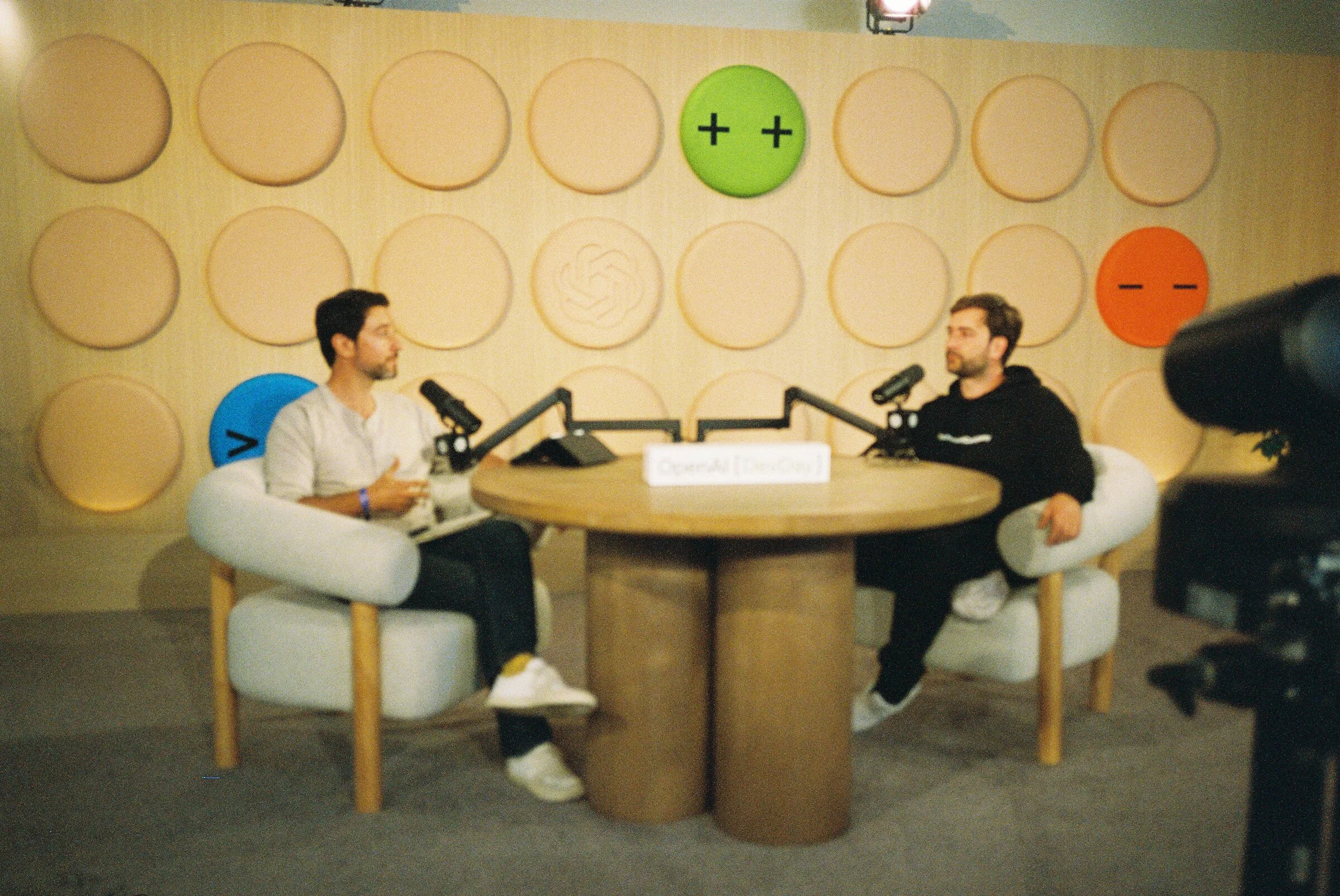 Two people talking at a round table on a podcast set with circular wall panels