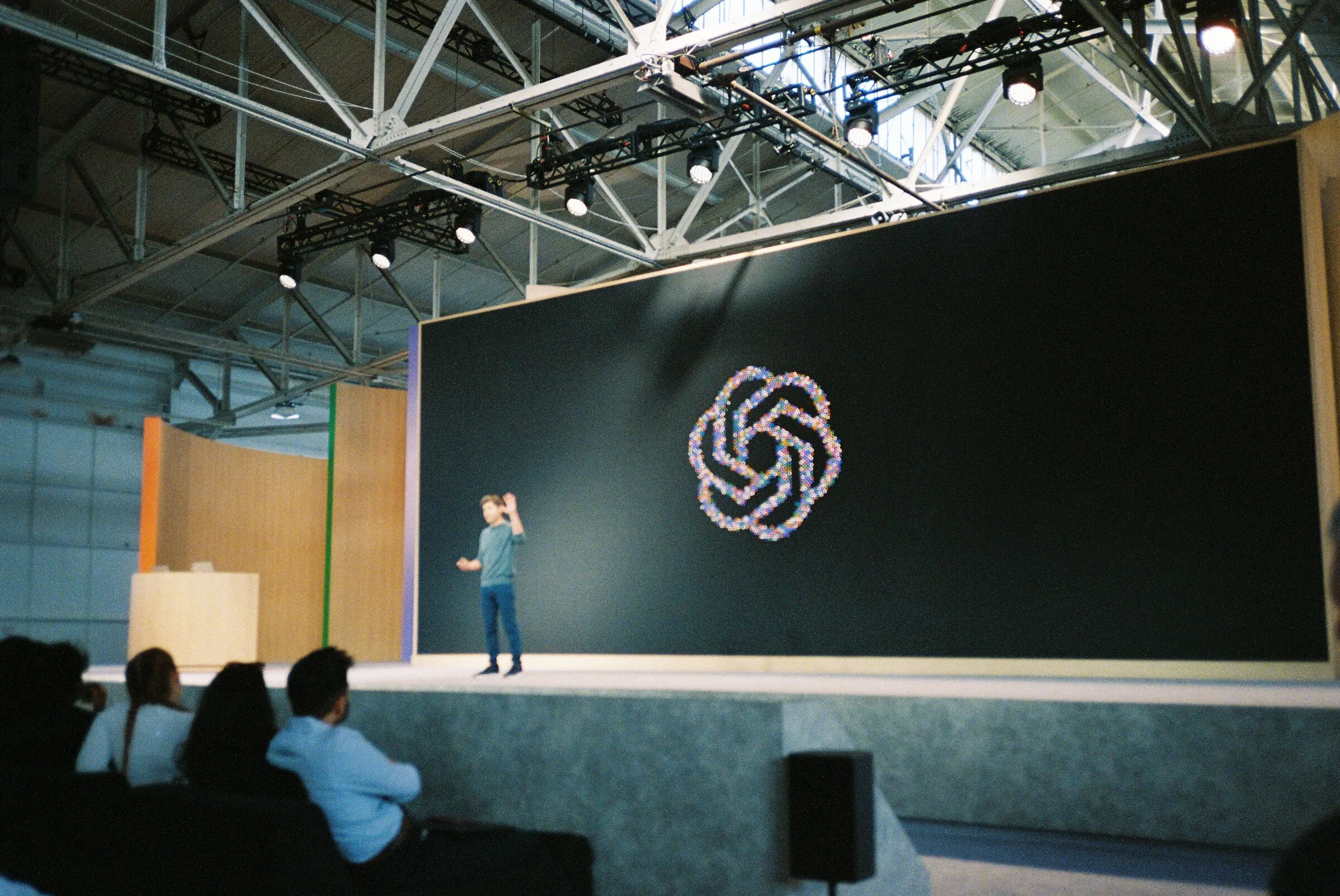 A presenter on a large stage beneath the OpenAI logo