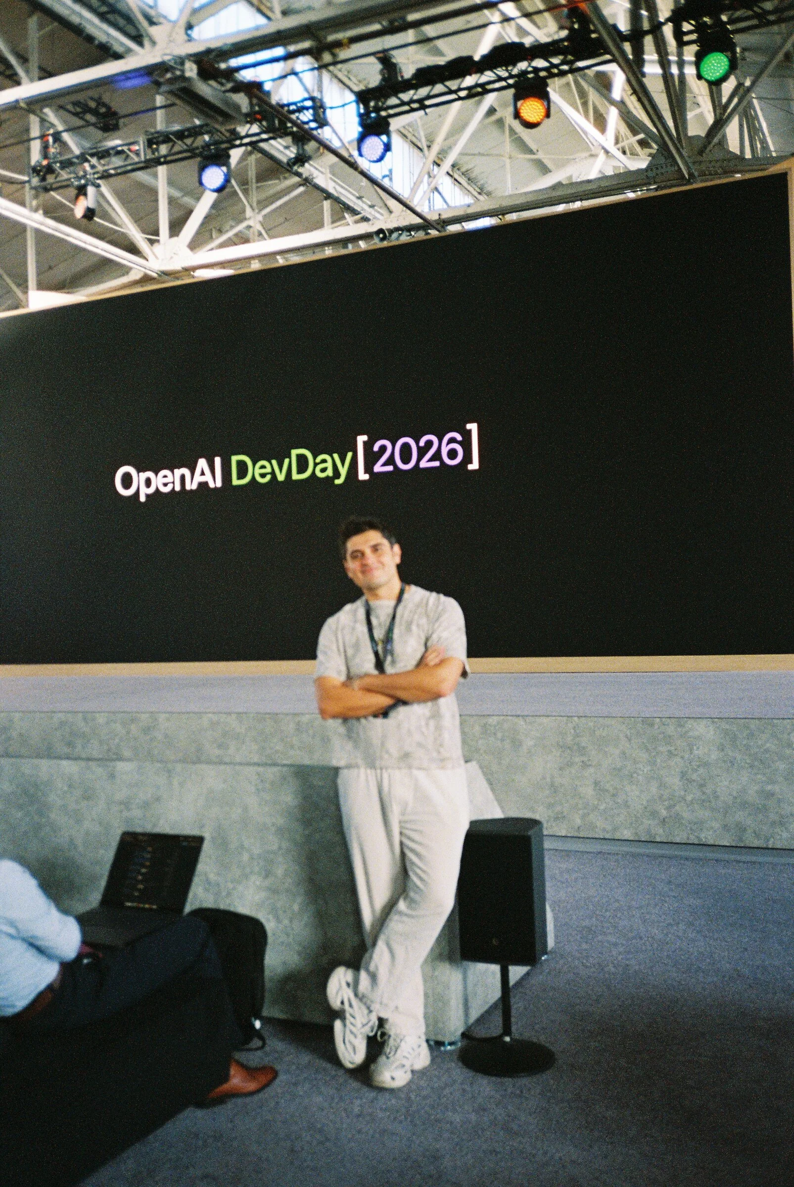 A man leaning against the stage edge beneath the DevDay 2026 screen
