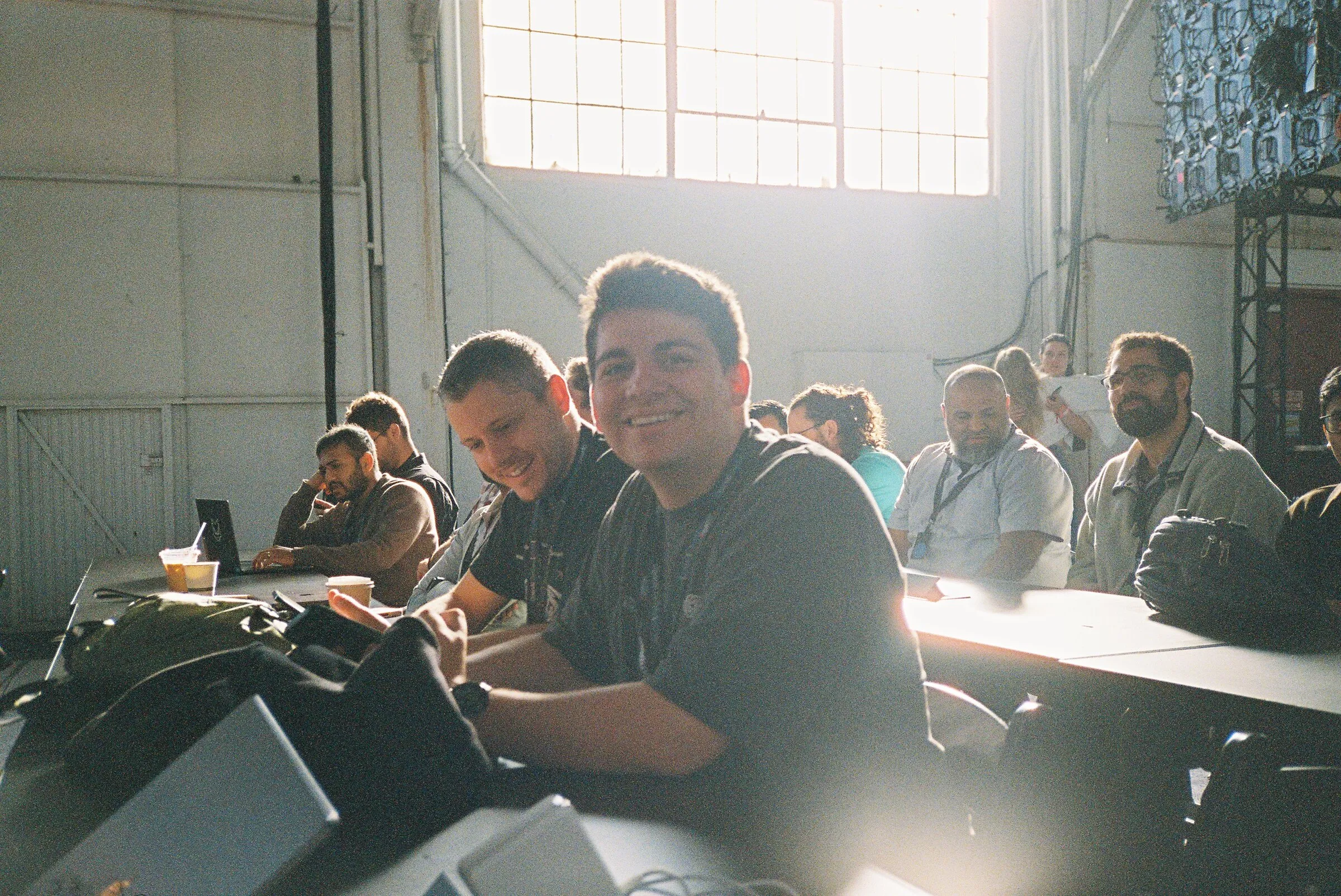 People working at a table, lit from behind by bright hangar windows