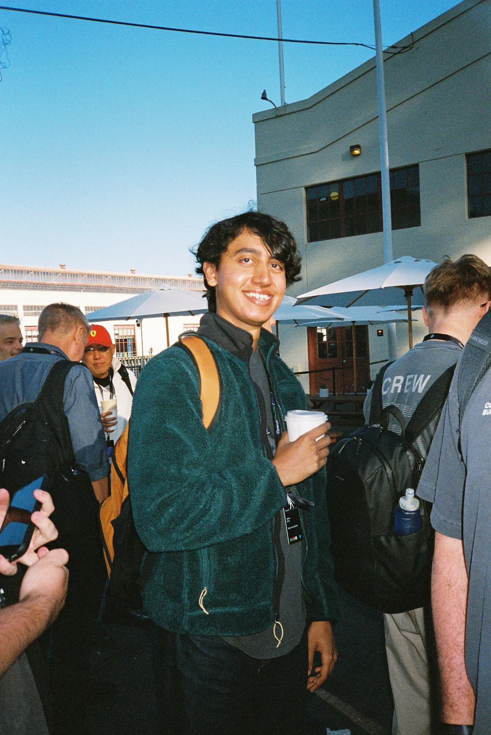 A smiling man in a green fleece holding a coffee cup in the sun