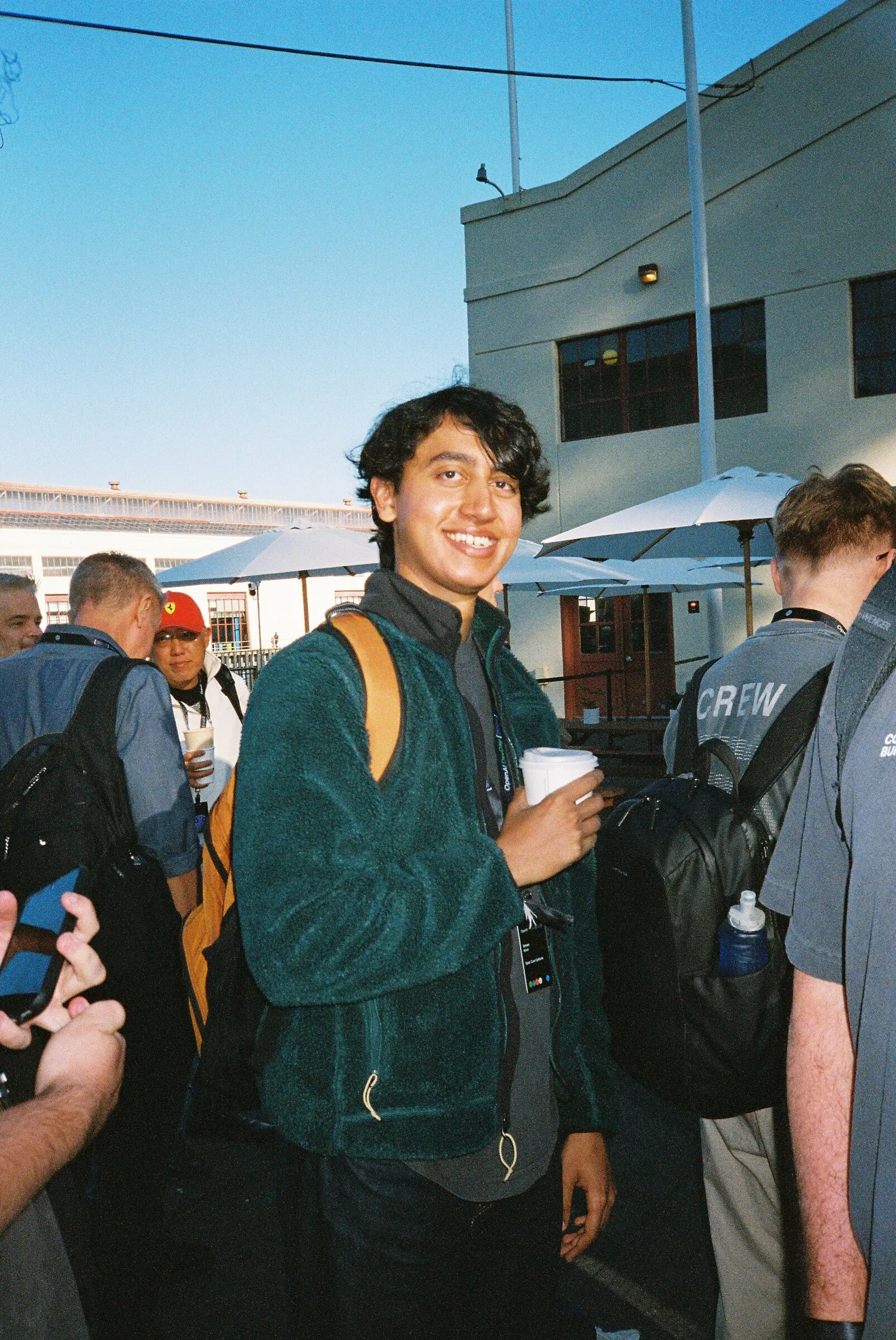A smiling man in a green fleece holding a coffee cup in the sun