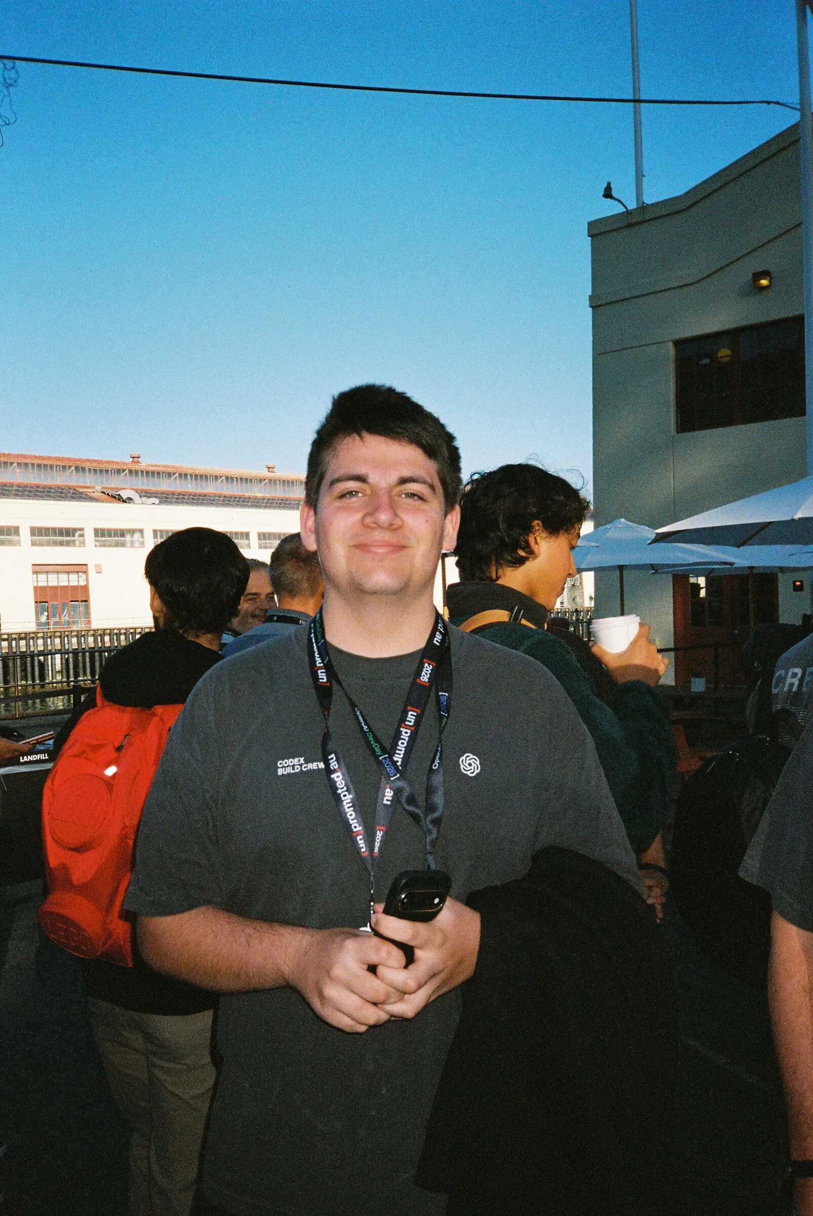 A smiling man in a grey t-shirt and lanyard in a courtyard