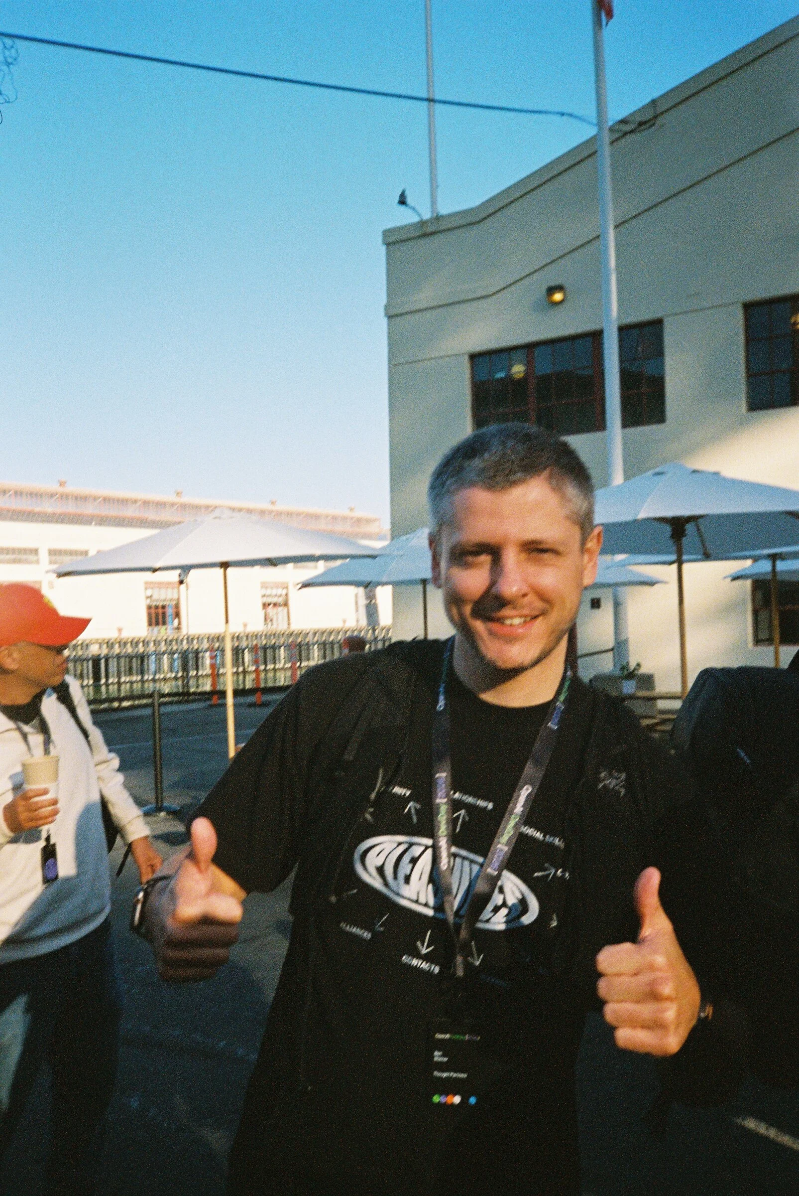 A man giving two thumbs up in a sunlit courtyard