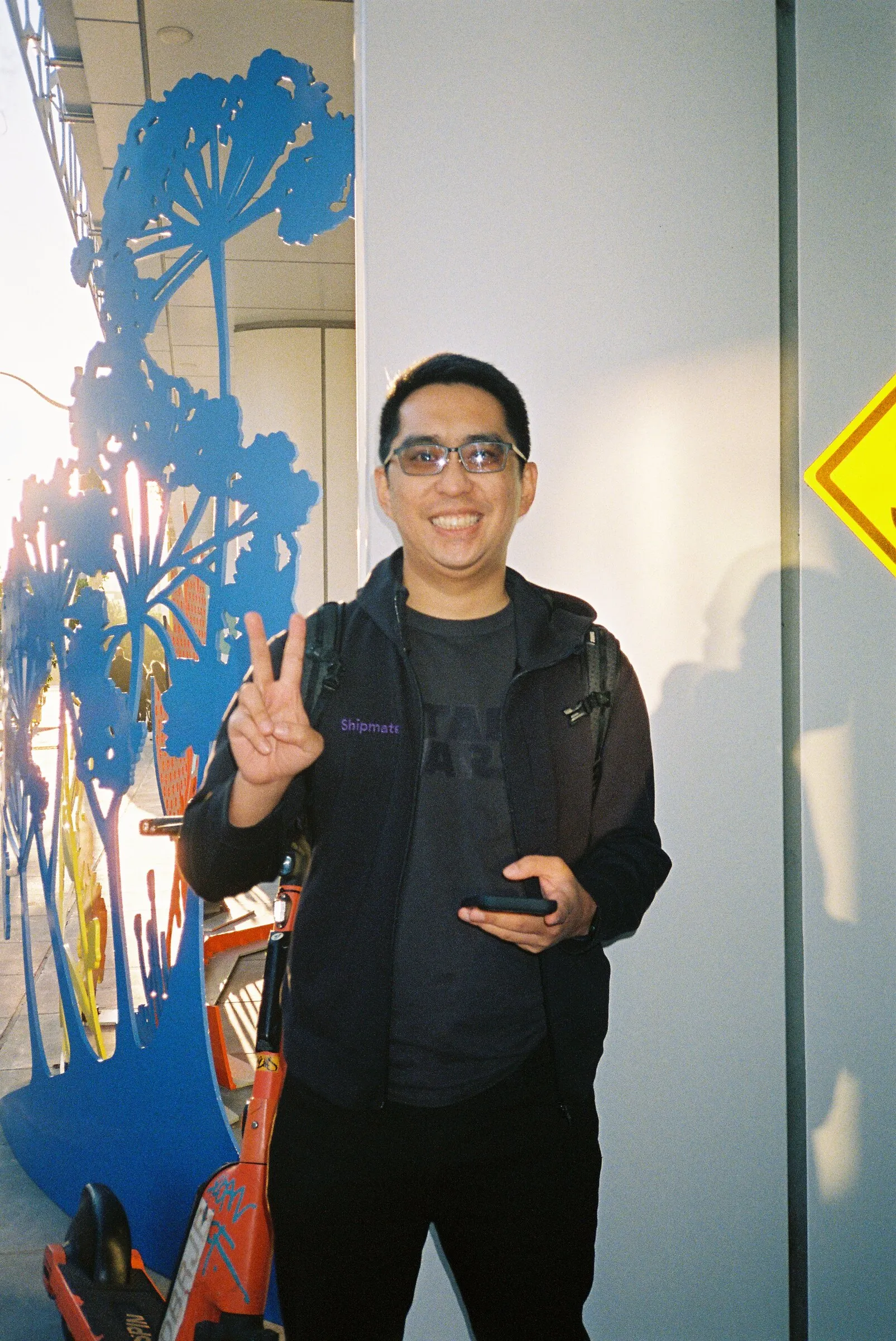 A smiling man giving a peace sign beside a blue floral mural