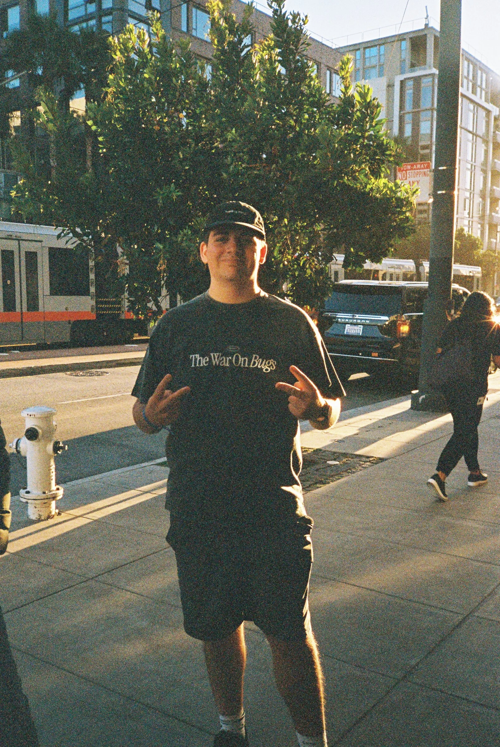 A man in a cap posing on a tree-lined street