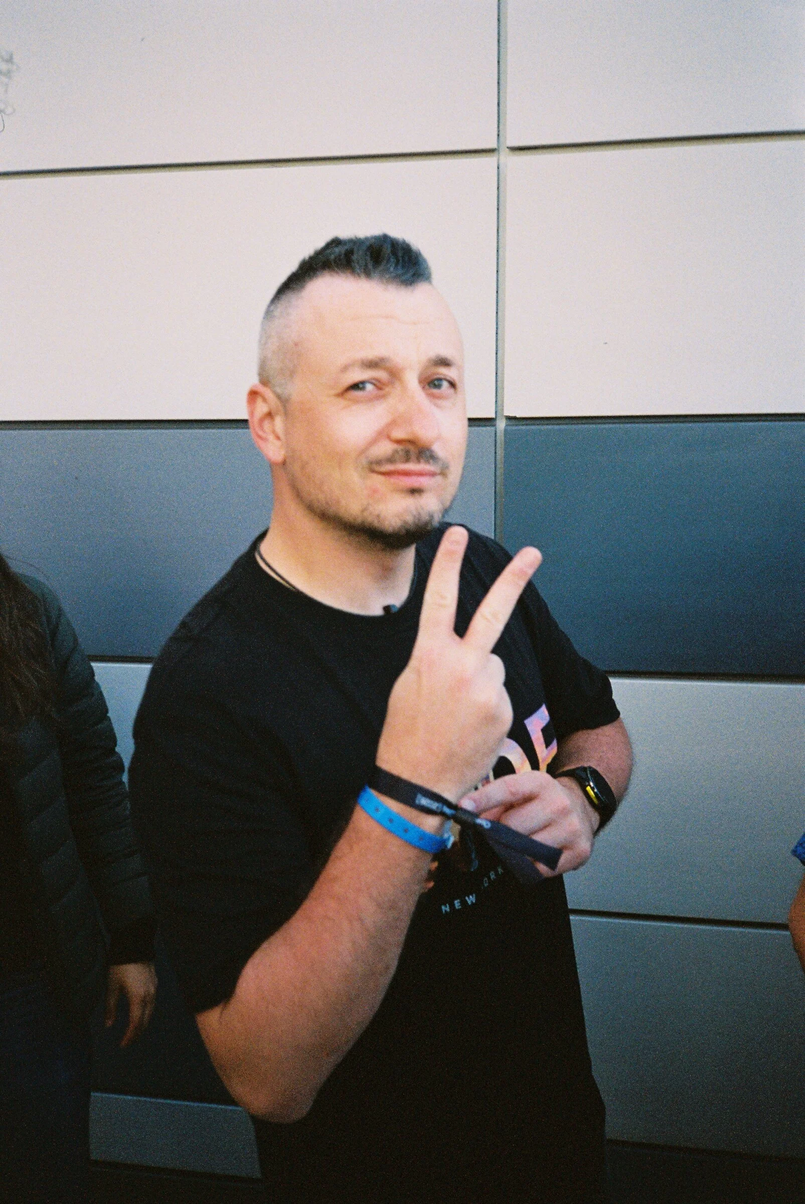 A man giving a peace sign against a grey panelled wall