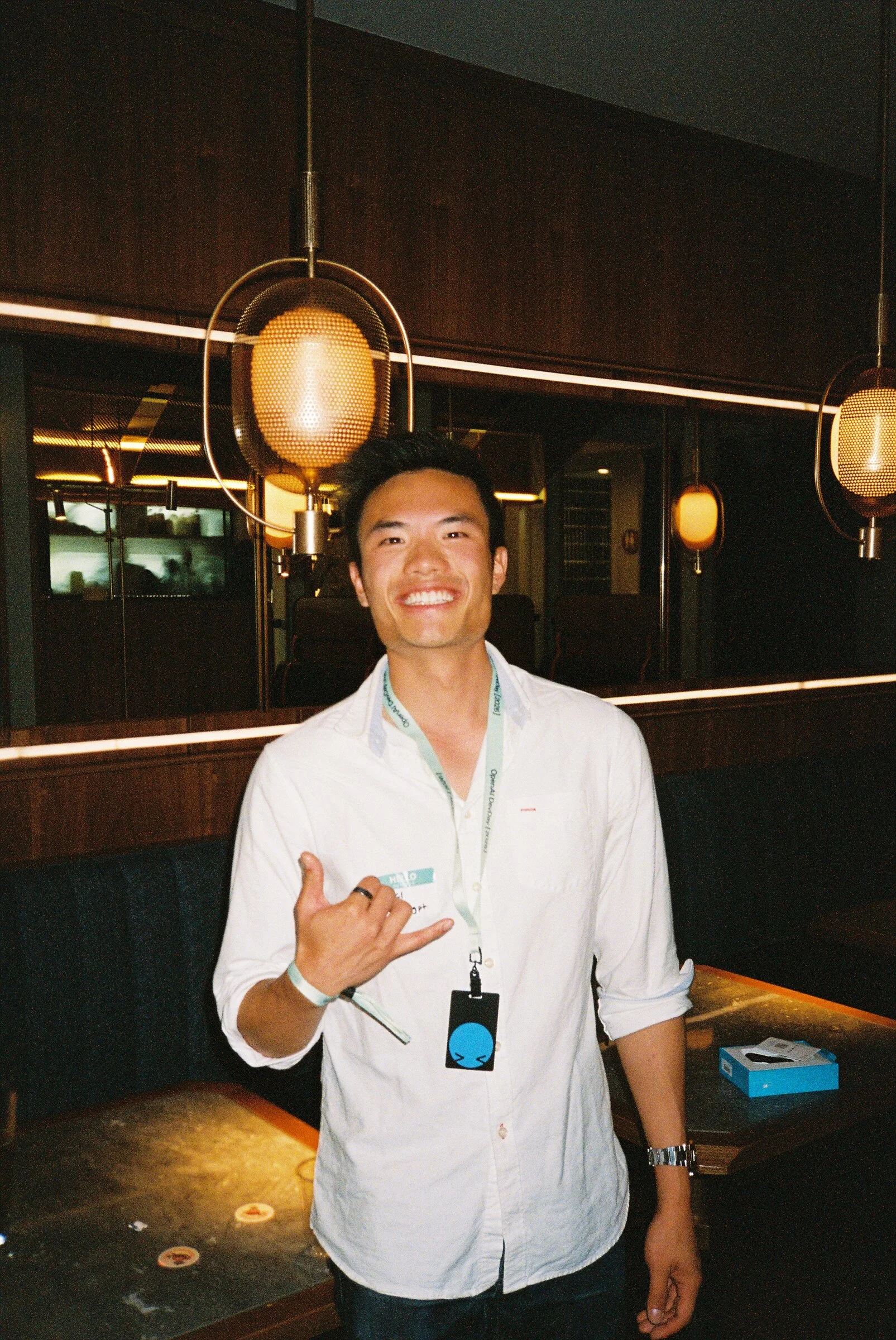 A man in a white shirt giving a shaka sign in a bar