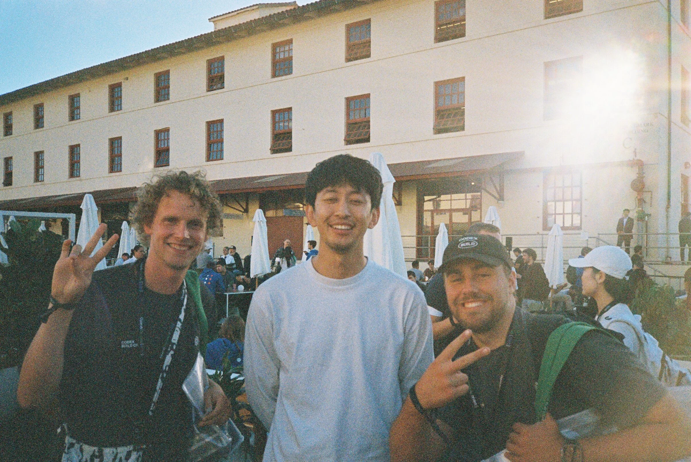 Three men smiling in front of a building at sunset
